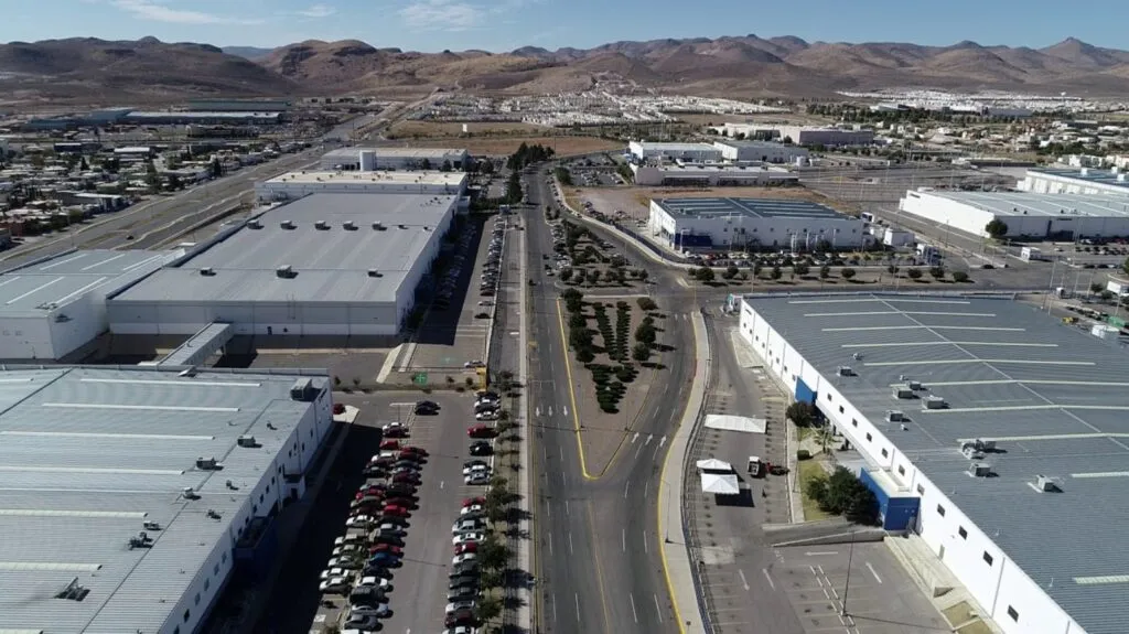 Vista aérea de parque industrial en Chihuahua con grandes naves de manufactura, estacionamientos llenos y zona urbana al fondo.