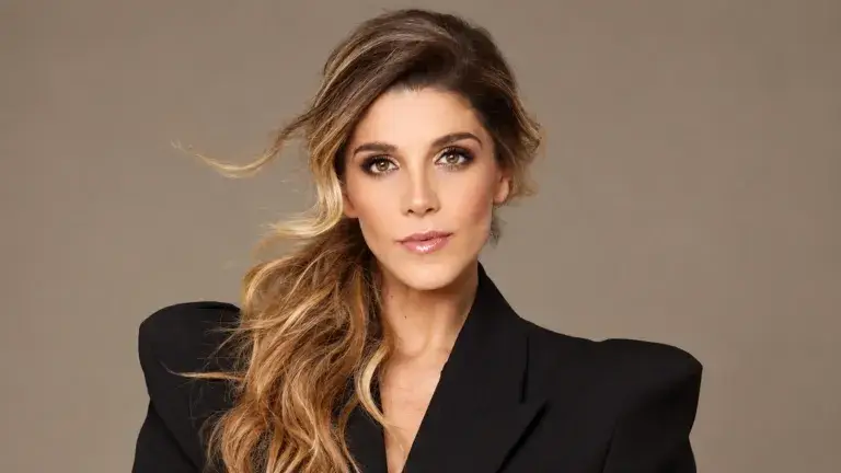 Retrato de Natalia Alcocer con saco negro y cabello ondulado sobre un hombro, frente a un fondo beige.